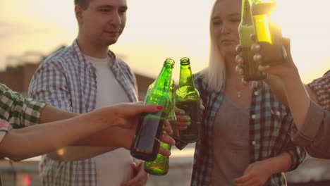 Young-people-clinks-glasses-and-drinks-beer-from-green-bottels-on-the-party-with-friends-on-the-roof